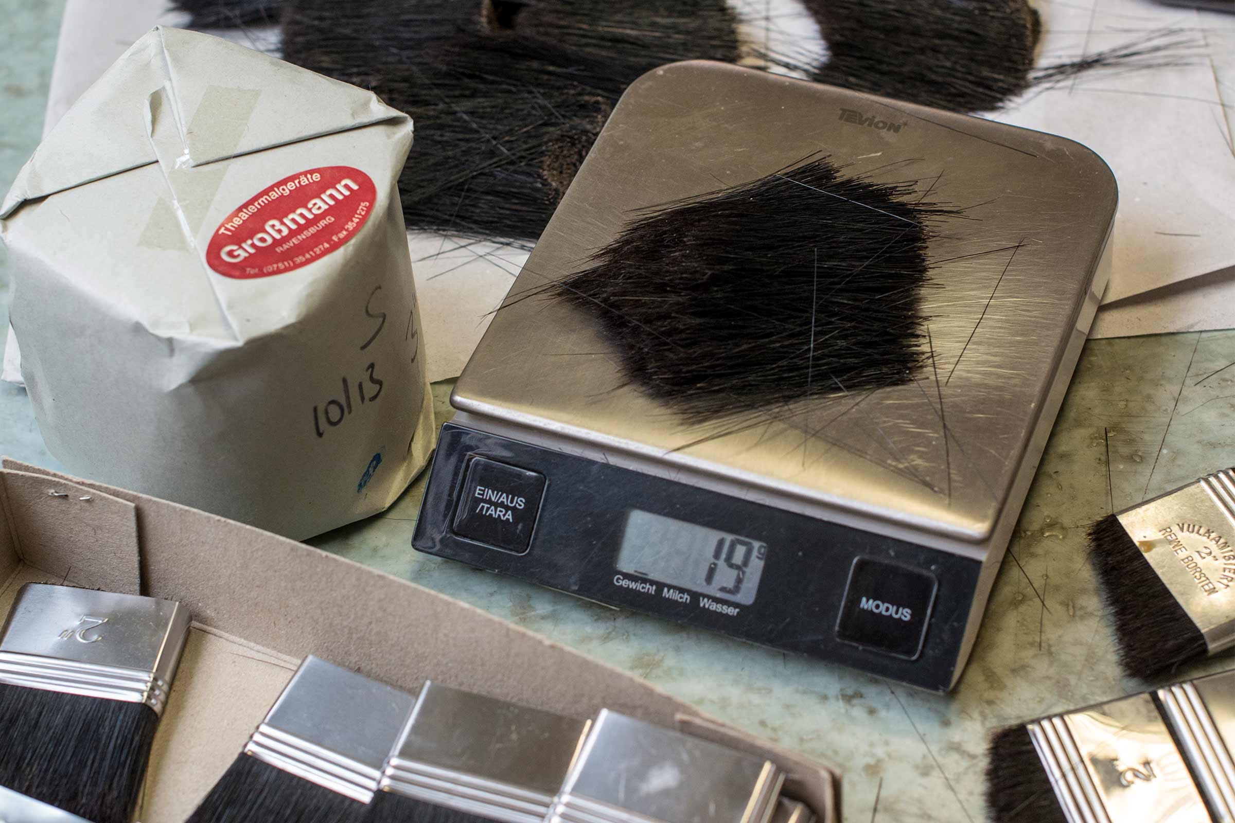 Bürstenhaare auf einer Waage, neben einer Verpackung und Pinseln