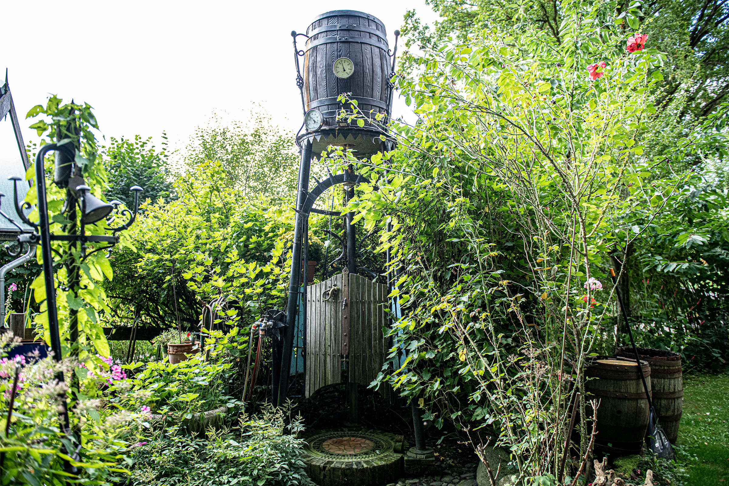 Gartenansicht mit dekorativer Fassdusche und üppiger Bepflanzung