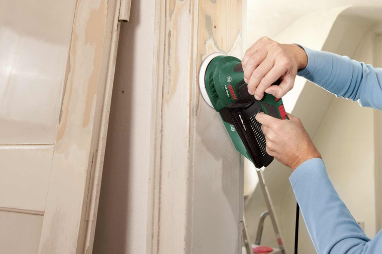 Eine Person schleift eine Holztür mit einem Exzenterschleifer von Bosch.