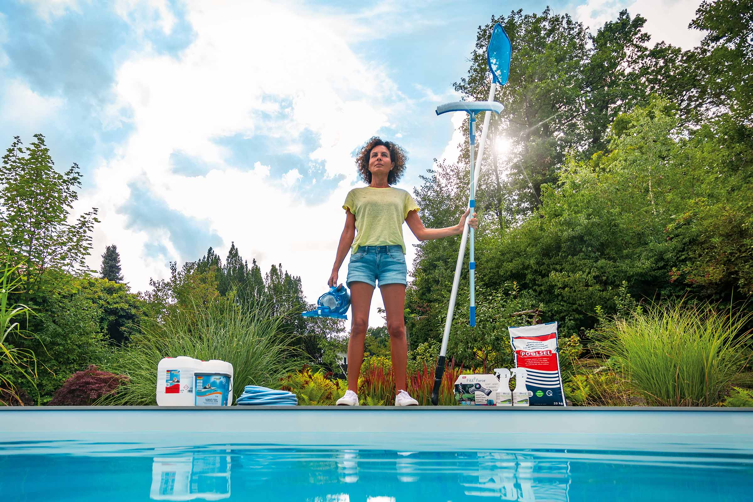 Frau mit Poolreinigungsset und Poolchemikalien am Pool