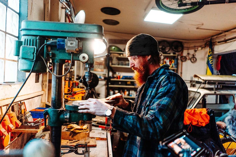 Atelier avec perceuse à colonne où un homme travaille une pièce.