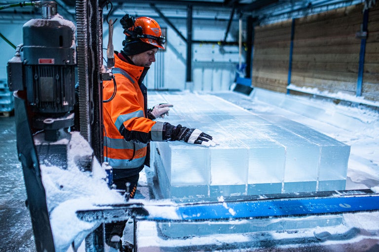 Ein Arbeiter mit Schutzhelm und Warnweste steht neben Eisblöcken.
