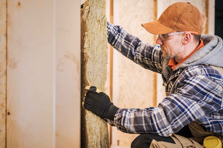 Un artisan installe de la laine d'isolation sur un mur en bois pour l'isolation thermique d'une maison.