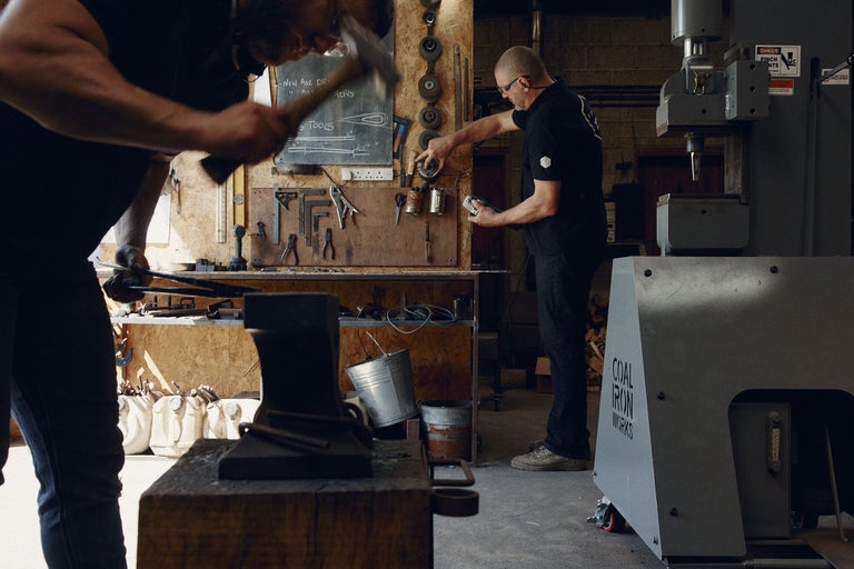 Werkstatt-Szene mit Amboss, Werkzeugen und zwei Handwerkern bei der Arbeit