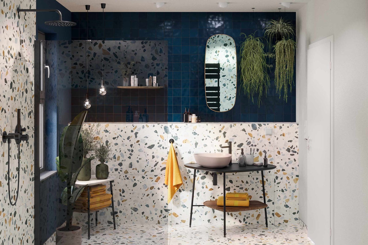 Salle de bain lumineuse avec sol en terrazzo, lavabo sur meuble-lavabo avec serviettes, douche et carreaux bleus