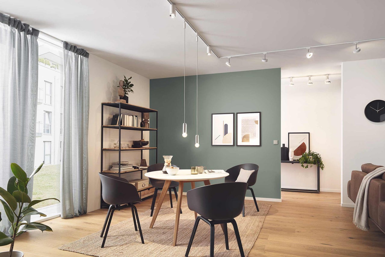 Salon lumineux avec table à manger, chaises, étagères, tableaux et système d'éclairage