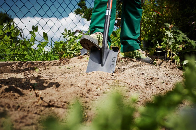 Scène de jardin avec une personne enfonçant une bêche dans le sol.
