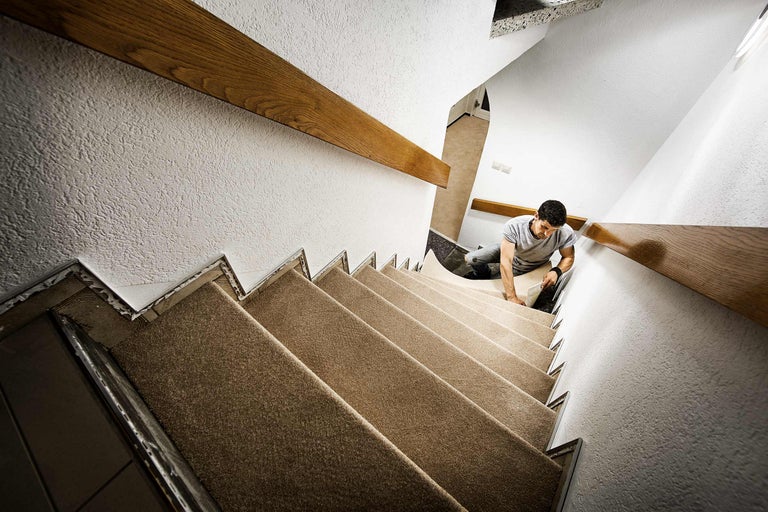 Mann verlegt Teppich auf einer Treppe mit Holzhandlauf.