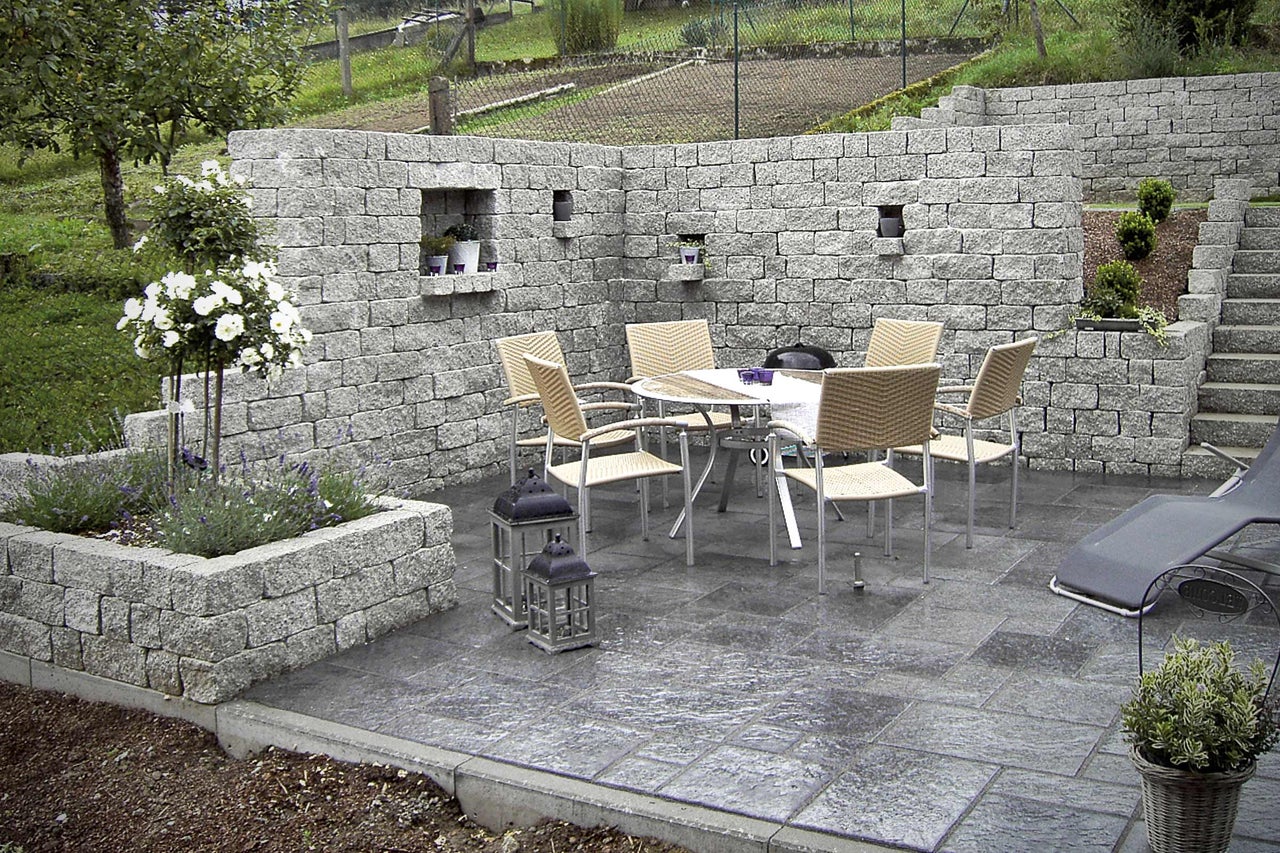 Espace de jardin aménagé avec mur en pierre, pavés, table, chaises et plantes