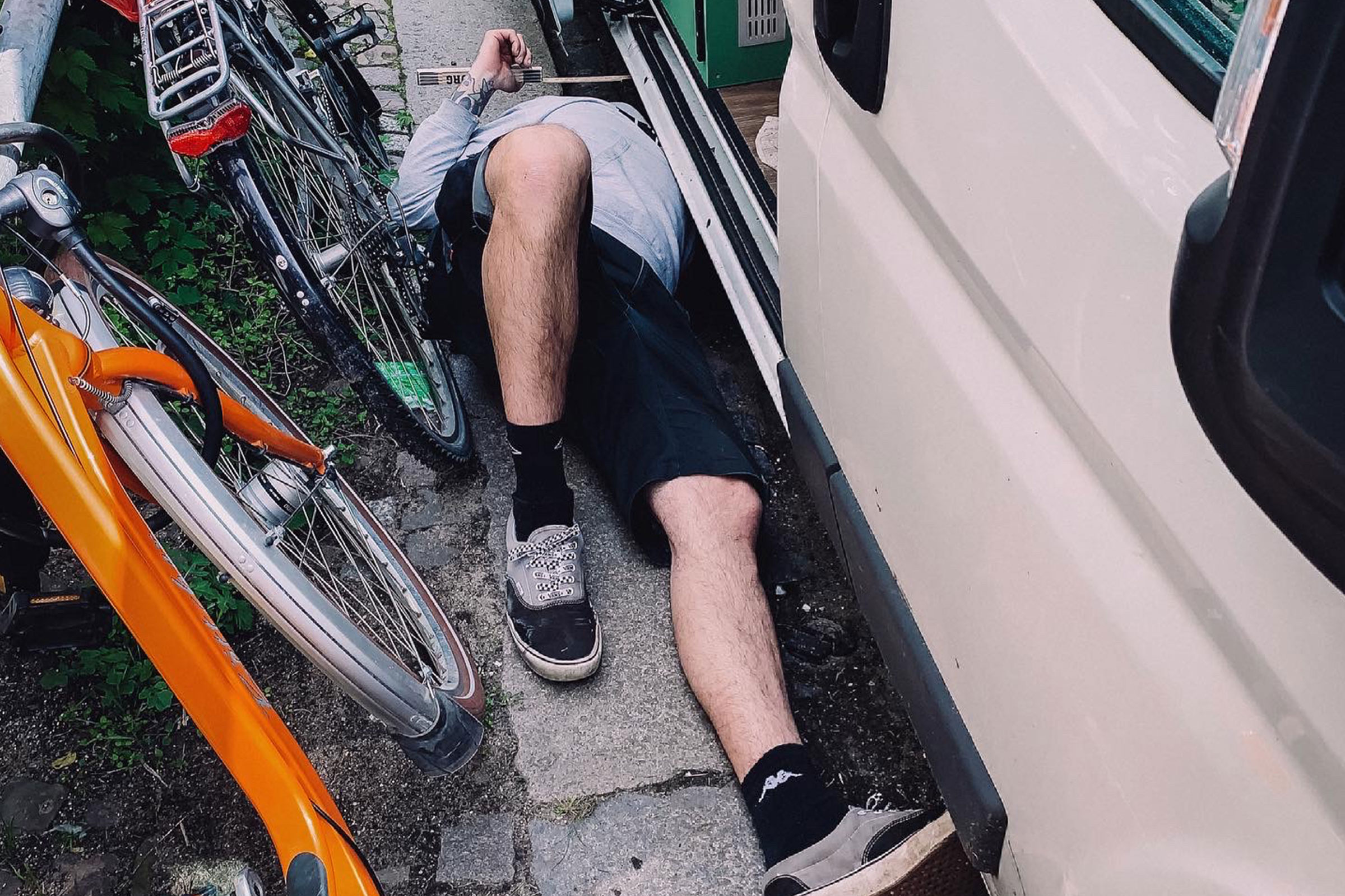 Eine Person liegt unter einem Fahrzeug, neben Fahrrädern.