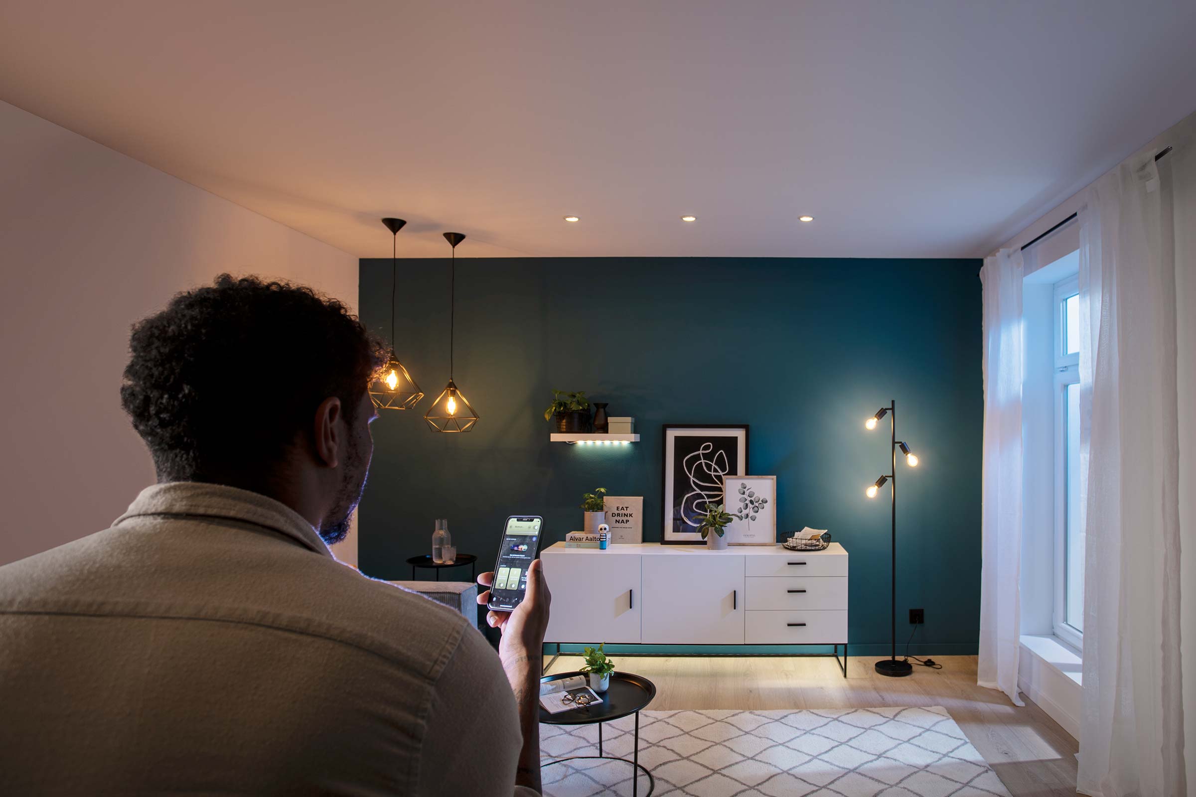 Mann steuert Beleuchtung im Wohnzimmer mit einer App auf seinem Smartphone