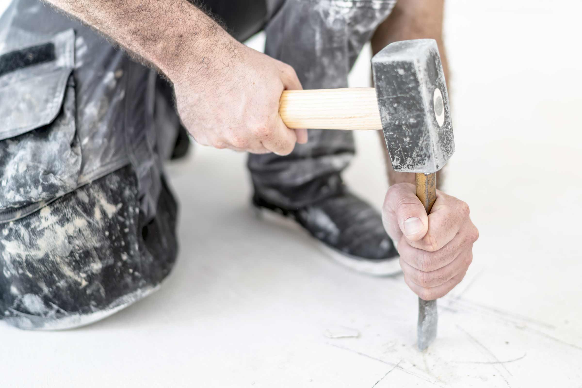 Handwerker bearbeitet Boden mit Hammer und Meißel