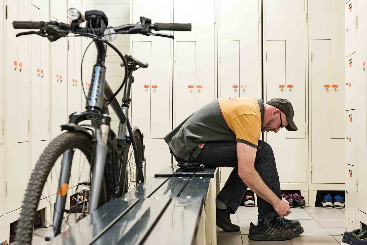 Un homme lace ses chaussures près d'un vélo dans un vestiaire avec des casiers.