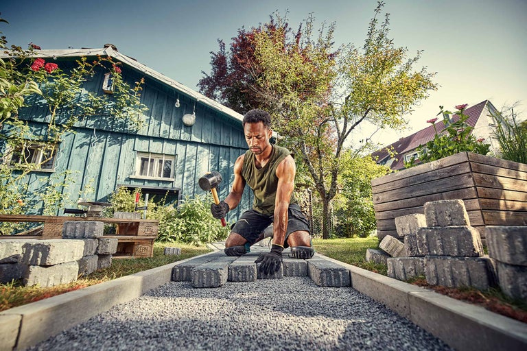 Un homme pose des pavés avec un maillet en caoutchouc dans le jardin