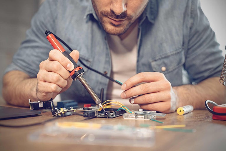 Mann lötet elektronische Bauteile mit einem Lötkolben auf einer Platine.