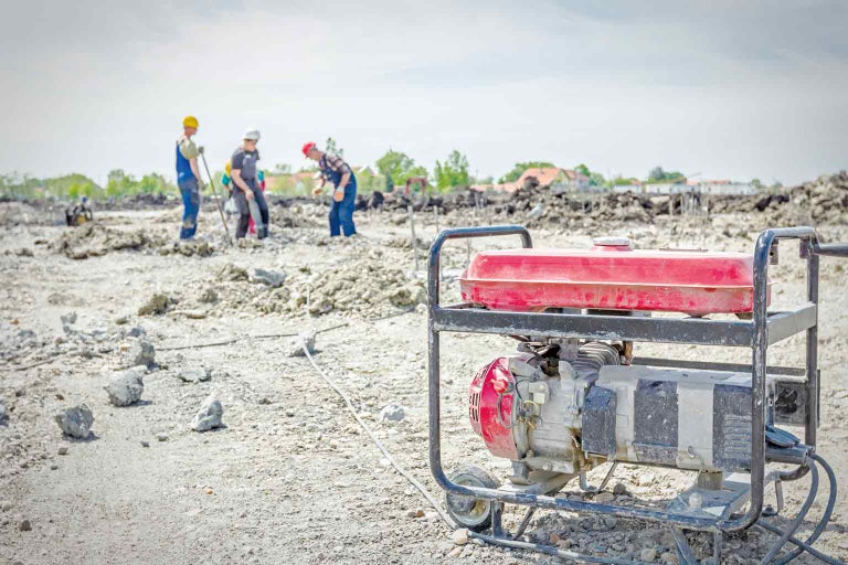 Stromerzeuger auf einer Baustelle mit Bauarbeitern im Hintergrund