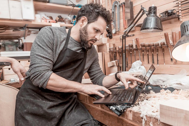 Un artisan portant un tablier utilise un ordinateur portable dans un atelier.