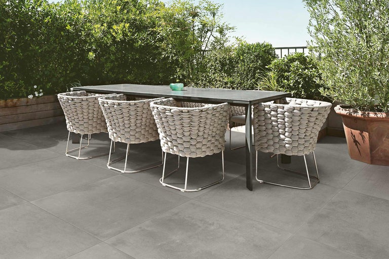 Table à manger avec chaises en osier sur dalles de terrasse grises dans le jardin