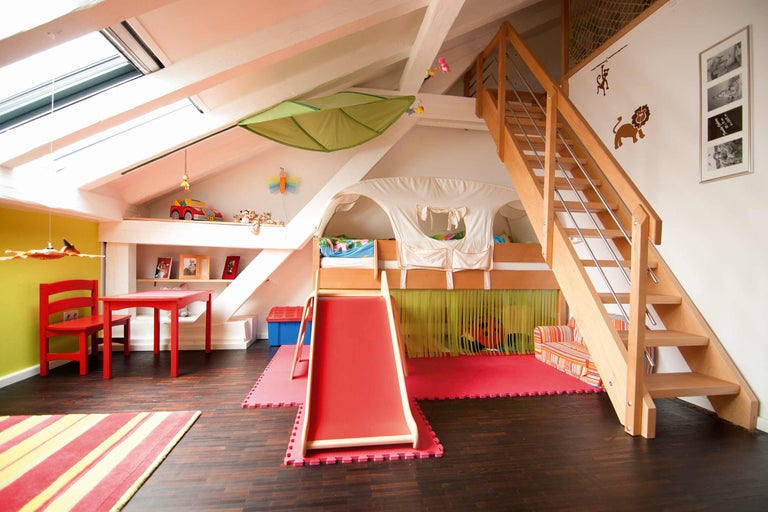 Chambre d'enfant avec lit mezzanine, toboggan, escalier, table de jeu et chaise.