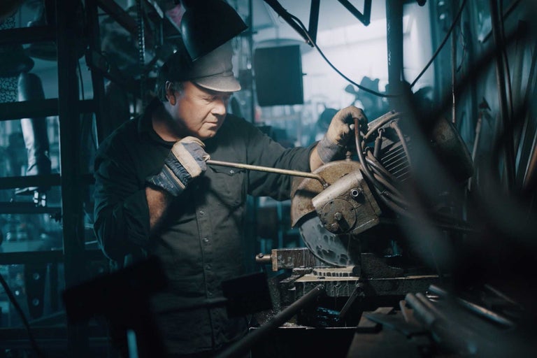 Ein Mann schneidet mit einer Metallsäge ein Metallstück ab, während er Schutzkleidung trägt.