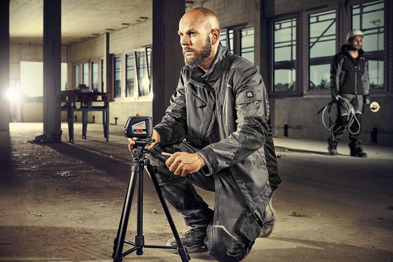 Un ouvrier est accroupi avec un laser lignes croisées et un trépied sur un chantier.