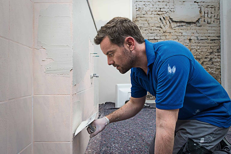 Un homme enduit des carreaux dans la salle de bain.