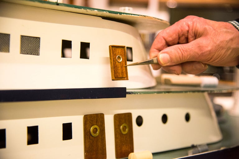 Detailaufnahme eines Schiffsmodells mit Pinzette, das ein kleines Holzstück hält