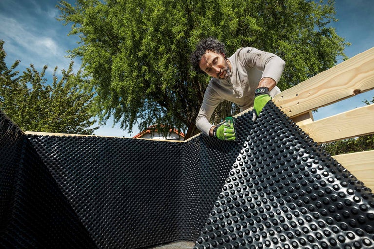 Un homme pose une membrane alvéolée dans un cadre en bois dans le jardin.