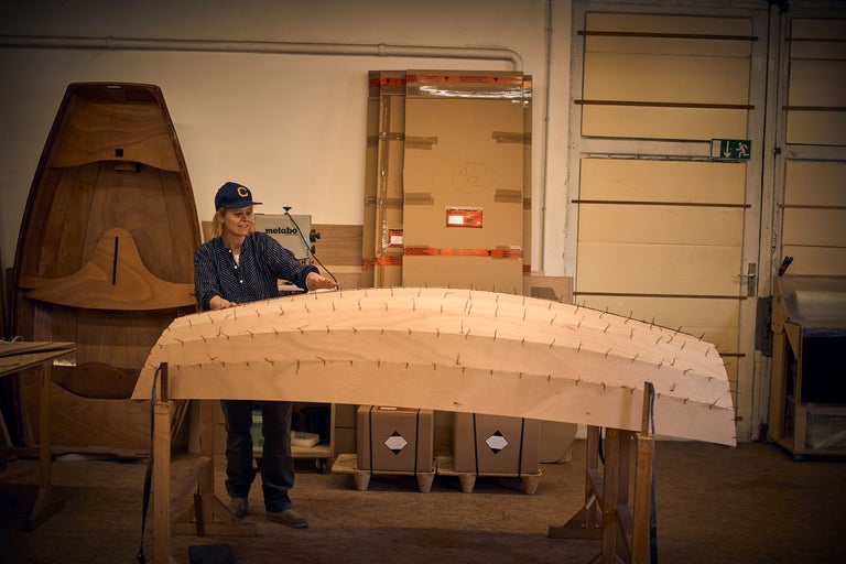 Une femme travaille sur un bateau en bois dans un atelier.