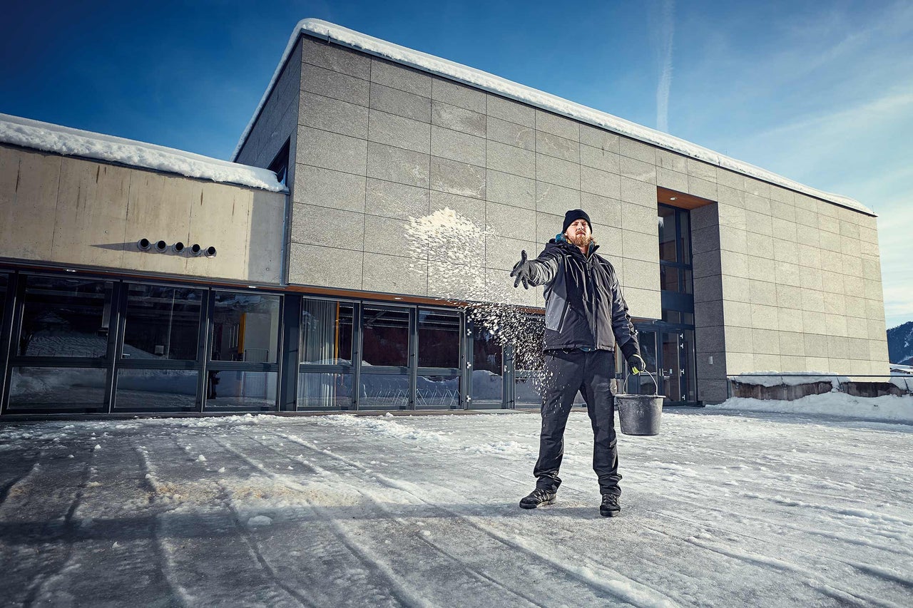 Un homme répand du sel de déneigement devant un bâtiment sur un sol verglacé