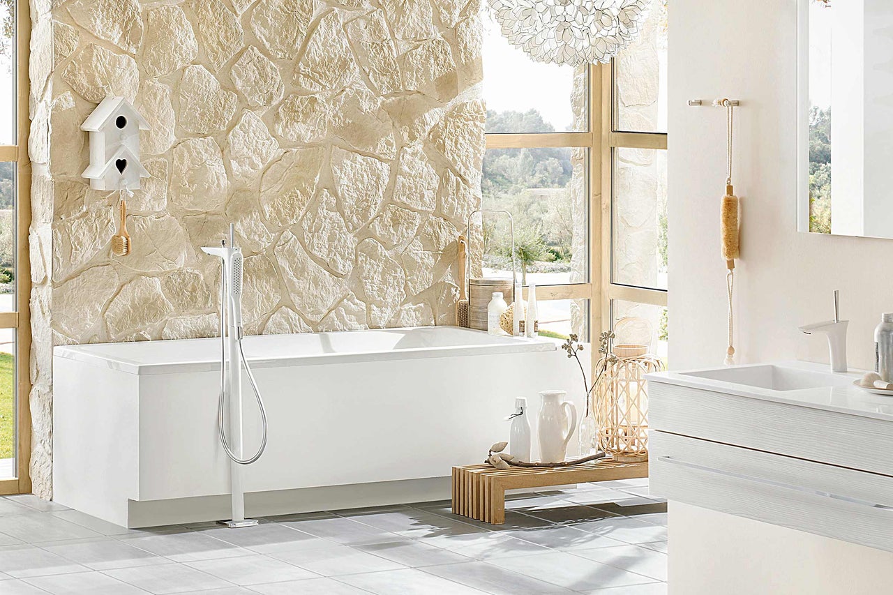 Salle de bain avec baignoire îlot, lavabo et mur en pierre