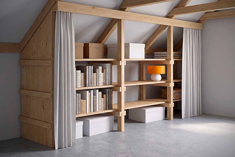 Étagère en bois avec des livres, des cartons, une lampe et un rideau dans une chambre mansardée
