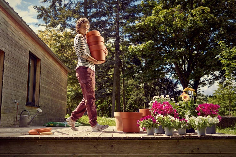 Femme portant des pots de fleurs dans le jardin sur une terrasse en bois