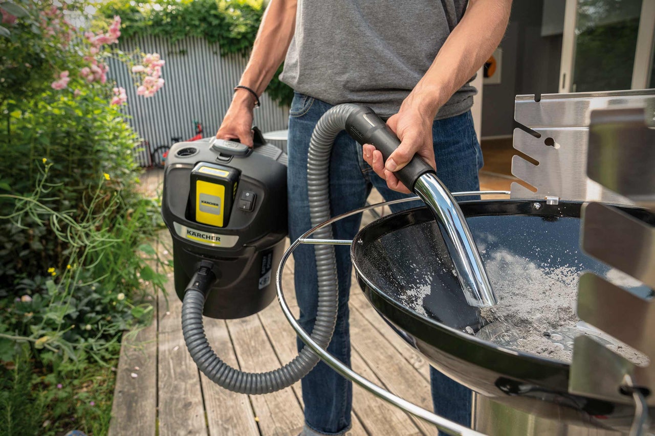 Une personne nettoie un gril avec un aspirateur de cendres Kärcher.