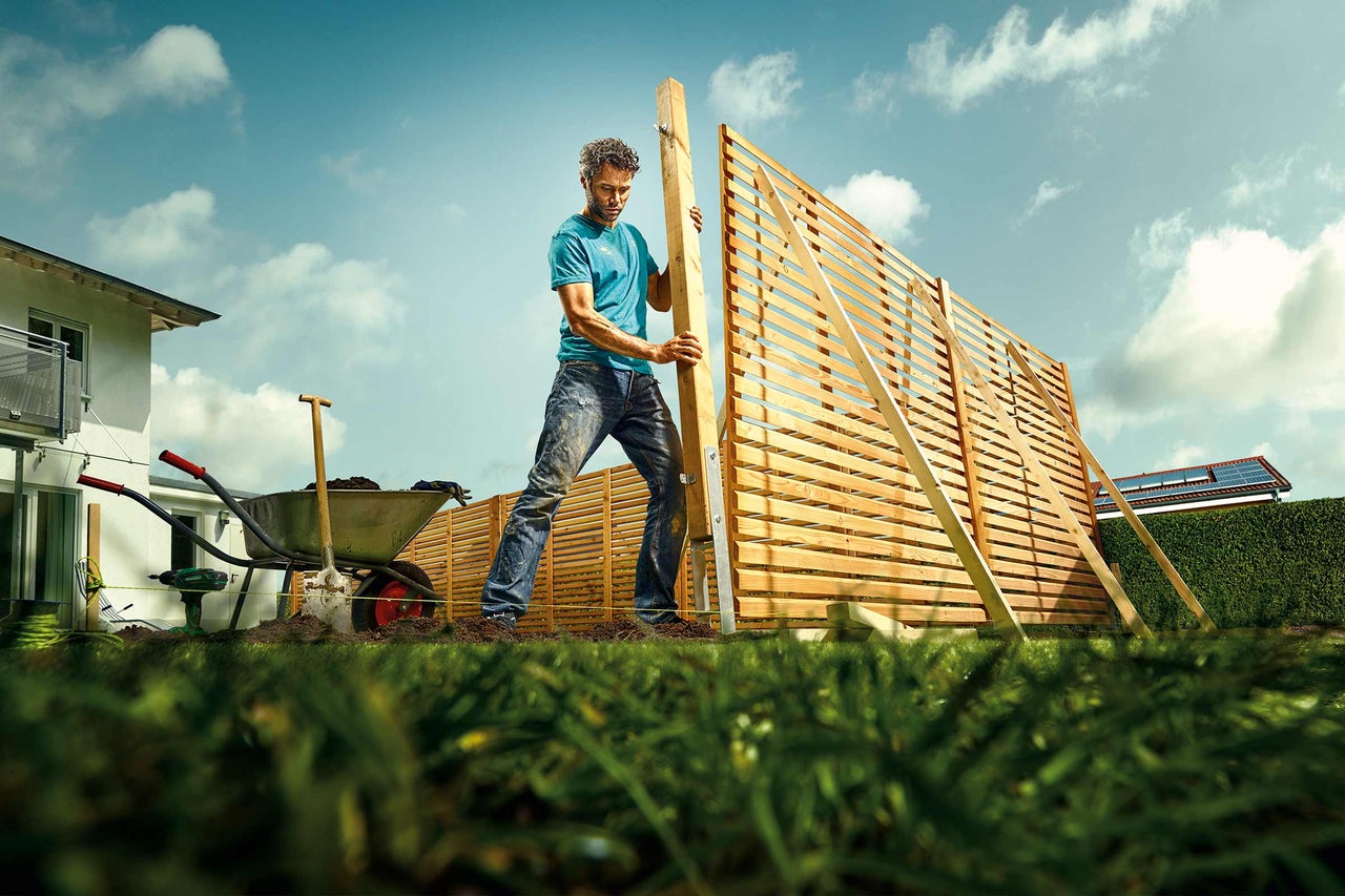Un homme installe un écran de confidentialité en bois dans le jardin.