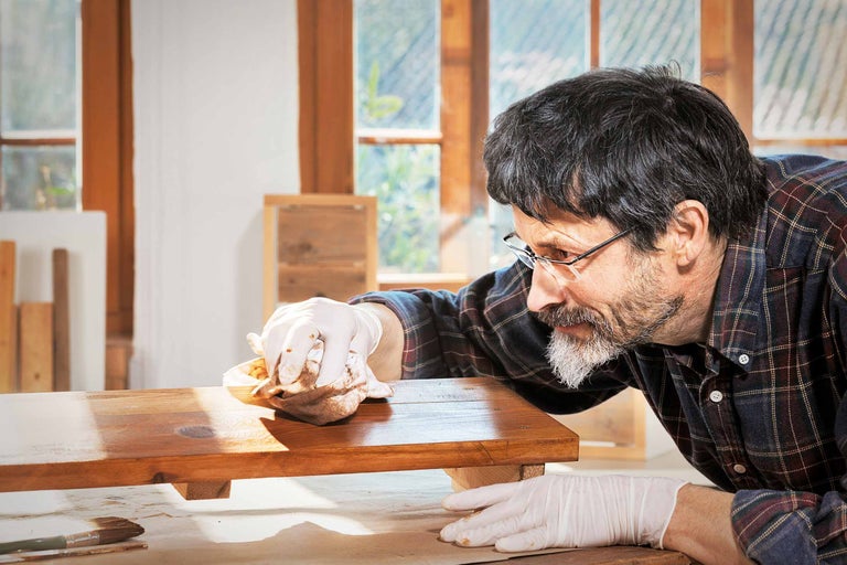 Un homme applique une lasure à bois avec un chiffon sur une pièce