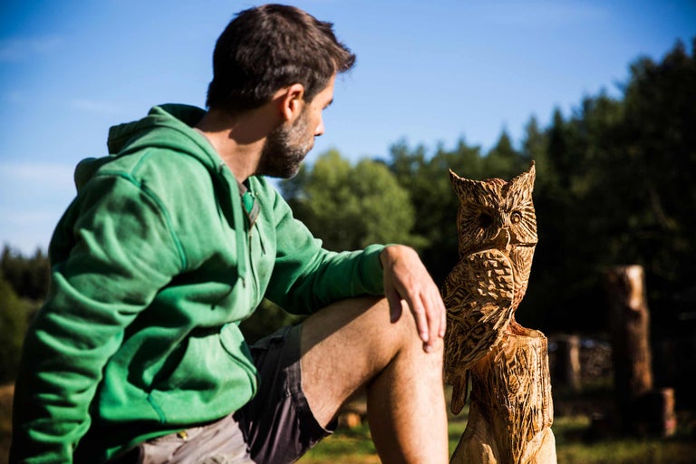 Un homme regarde une chouette en bois sculpté