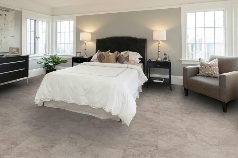 Schlafzimmer mit Bett, Nachttischen, Kommode, Sessel und Bodenbelag in Steinoptik für ein helles und freundliches Ambiente.