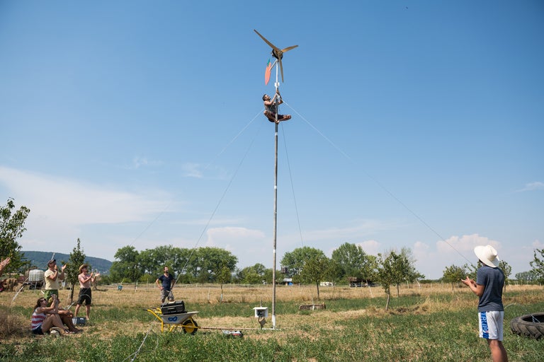 Eine Person klettert auf eine Windkraftanlage, während eine Gruppe von Leuten zusieht.