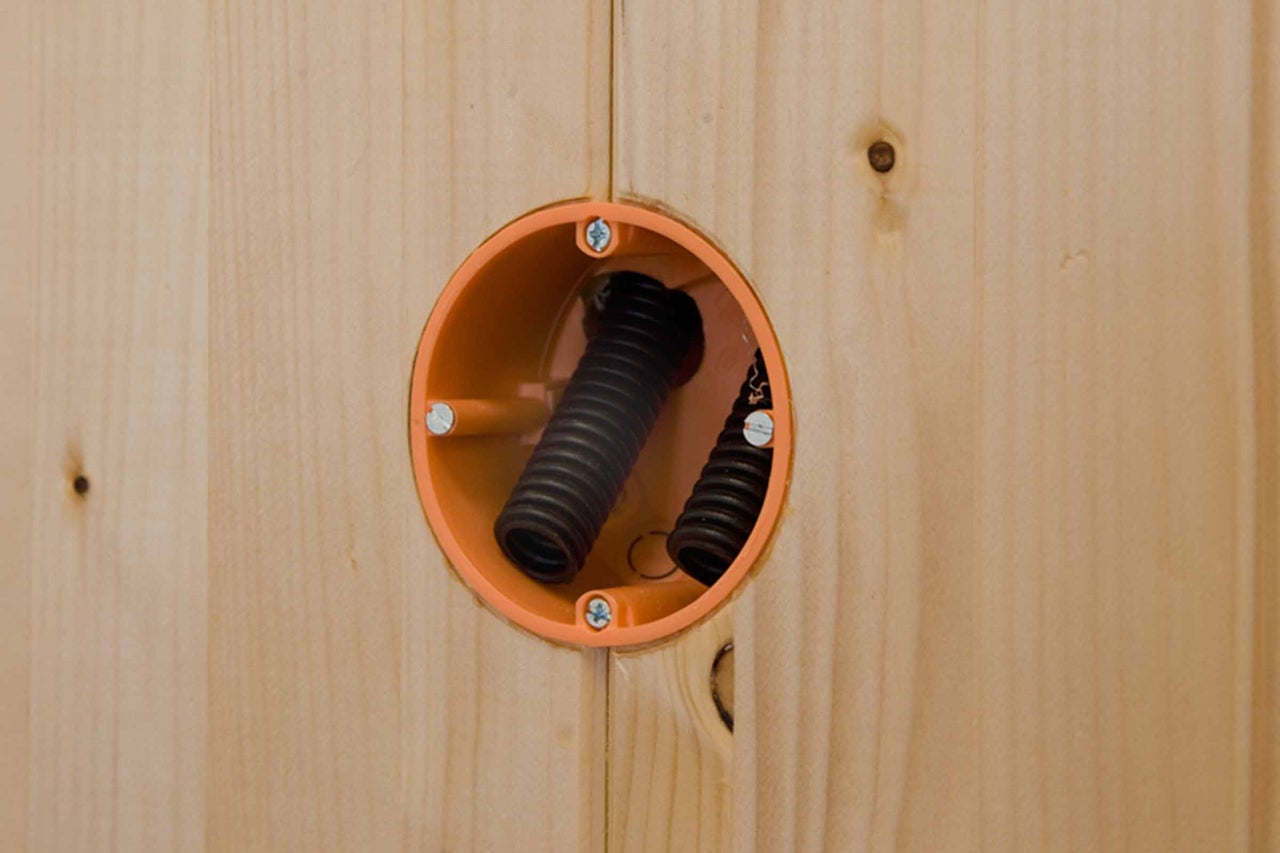Boîte pour cloisons sèches installée dans un panneau en bois avec deux gaines annelées noires pour l'installation électrique.