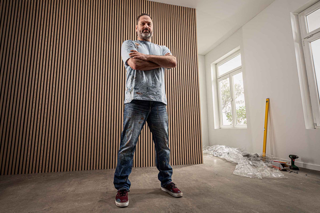 Mann steht vor einer Wand aus Holzpaneelen in einem hellen Raum.