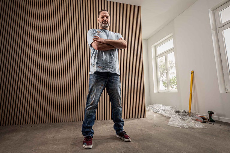 Mann steht vor einer Wand aus Holzpaneelen in einem hellen Raum.