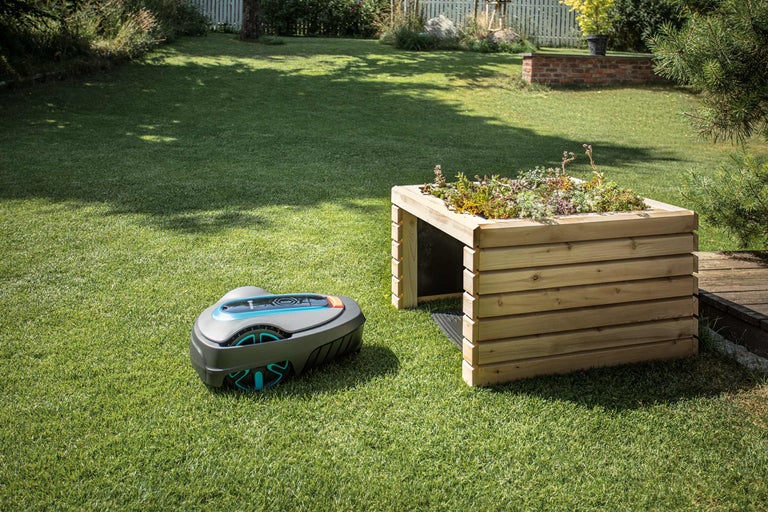 Scène de jardin avec robot tondeuse et table de plantation en bois.
