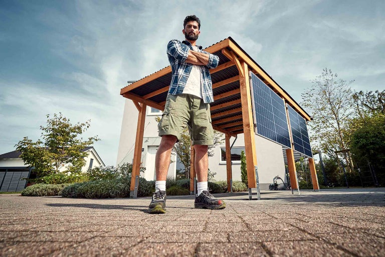 Homme les bras croisés devant un carport avec des panneaux solaires