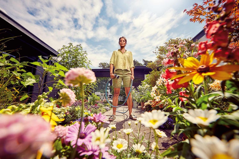 Femme arrosant les fleurs dans le jardin avec un tuyau d'arrosage.