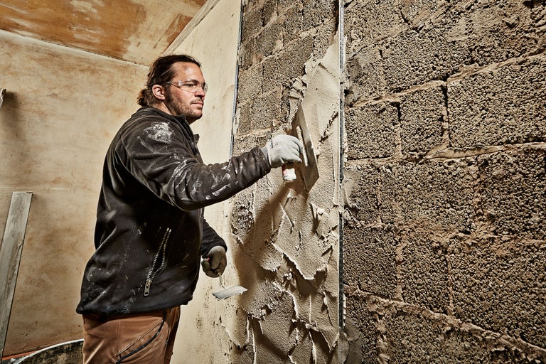 Un artisan enduit un mur de briques avec une truelle.