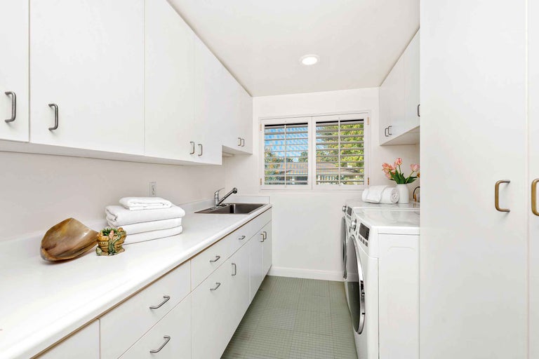 Buanderie lumineuse avec lave-linge, sèche-linge, évier et armoires blanches