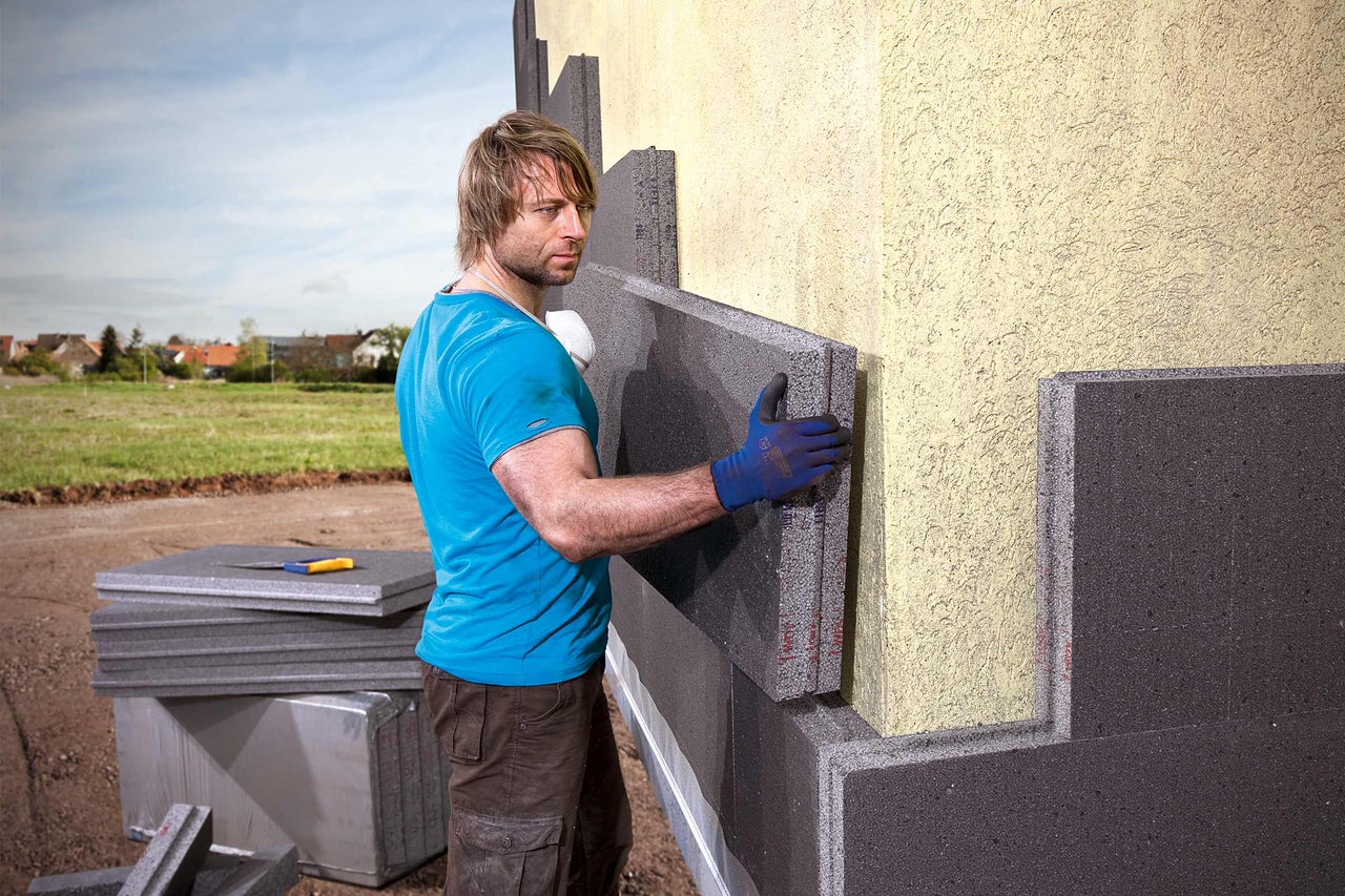 Un homme pose des panneaux d'isolation de façade sur un mur de maison