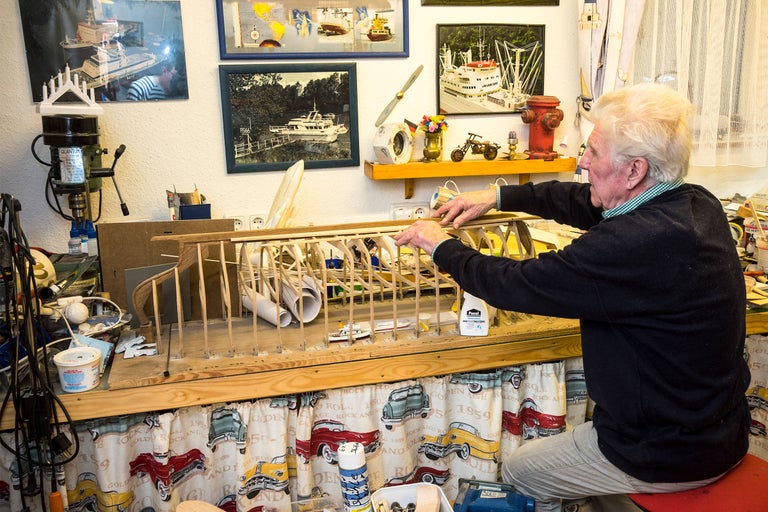 Mann baut ein Holzmodellflugzeug in seiner Werkstatt mit Werkzeug und Bildern an der Wand
