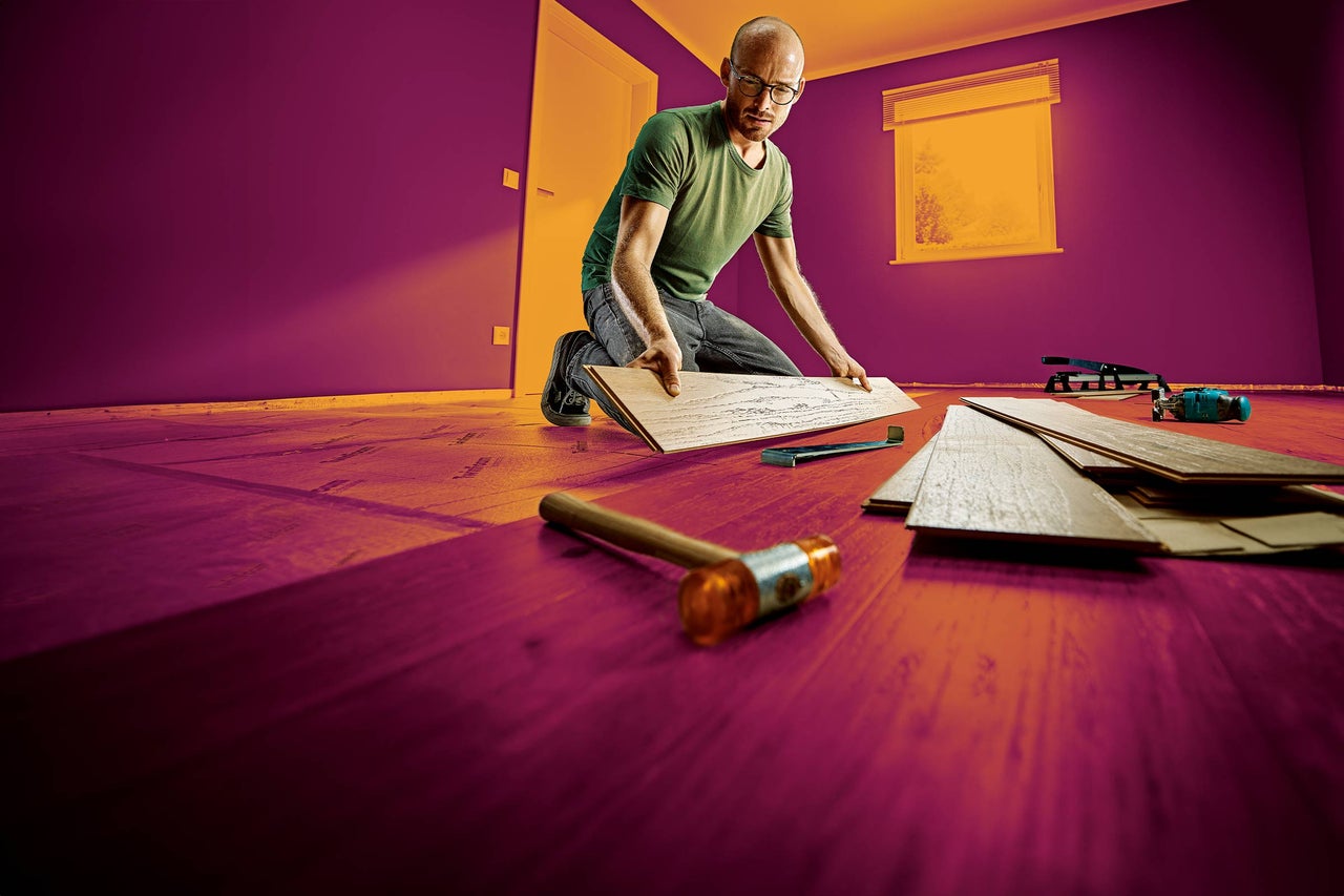 Un homme pose un sol stratifié dans une pièce avec des outils.